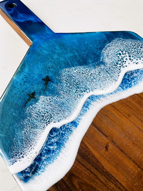 Two blue resin art waves on a srving board with two sharks swimming through the waves
