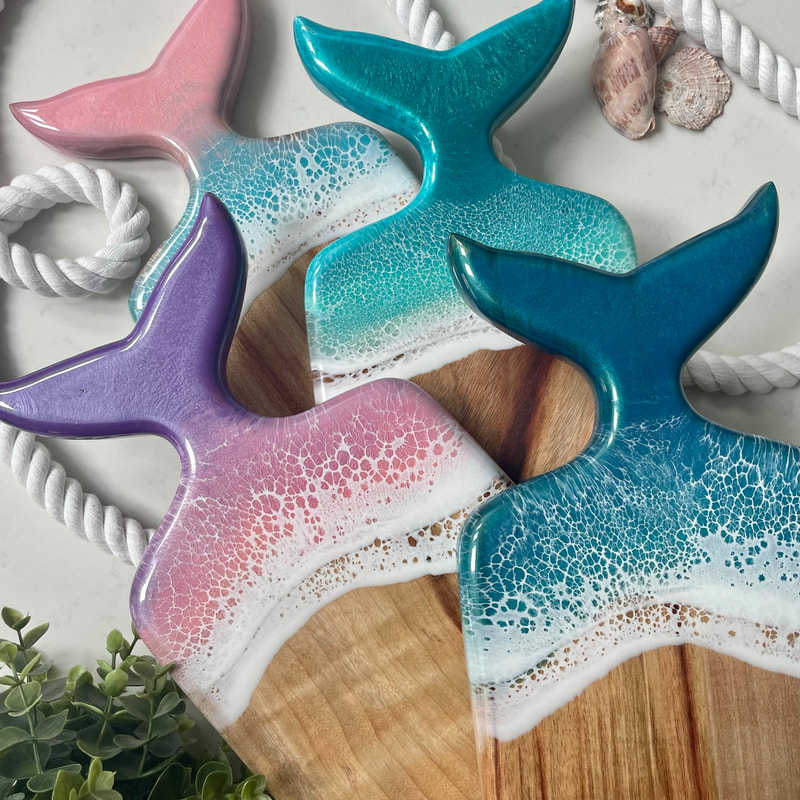 Four whale tail serving boards with different colours on the end of each tail